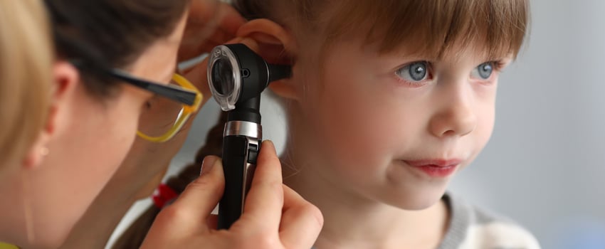 Woman physician looking into the ear of a young girl using an otoscope